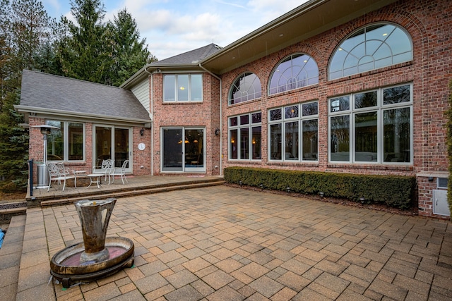 rear view of house with brick siding, roof with shingles, and a patio area