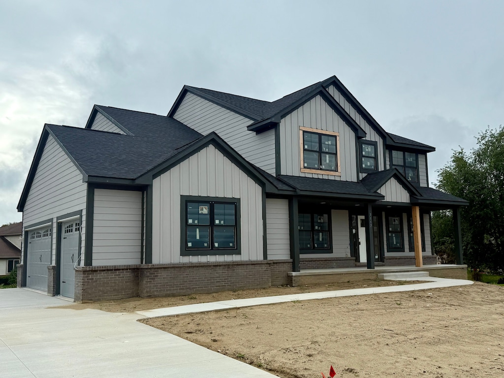 modern farmhouse with a garage, driveway, brick siding, and board and batten siding