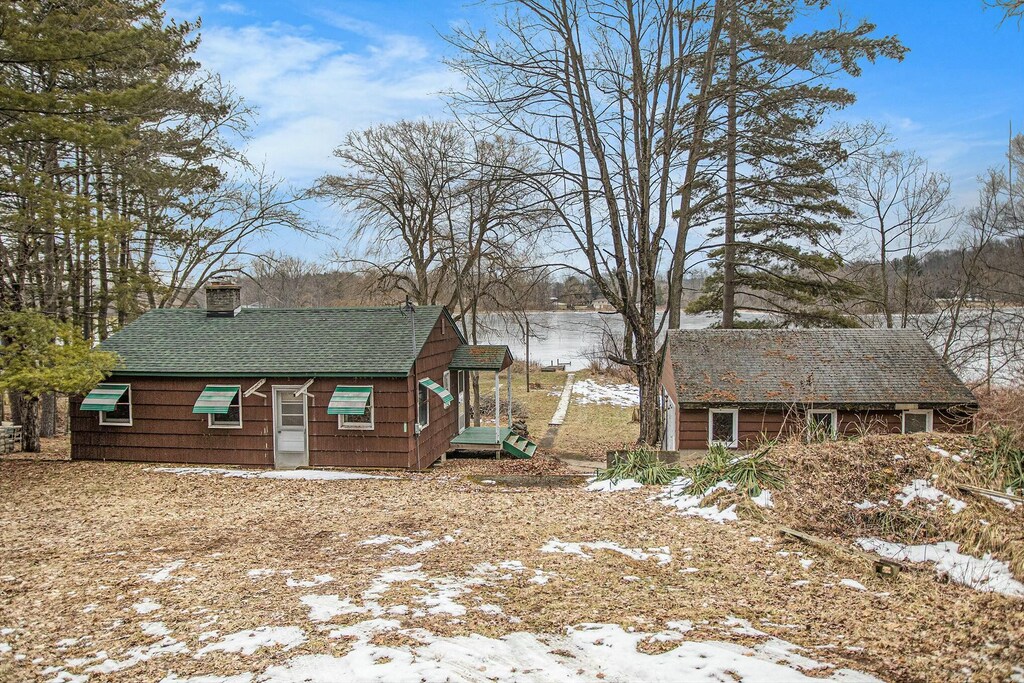 snow covered property with a shingled roof, a chimney, and an outdoor structure