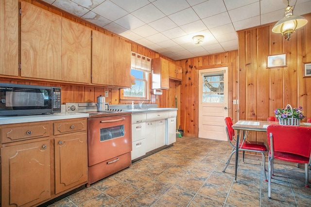 kitchen with light countertops, a sink, wooden walls, black microwave, and range