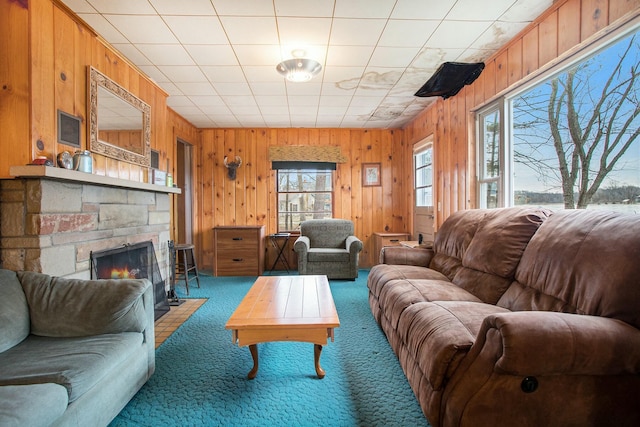 carpeted living room featuring wooden walls and a stone fireplace