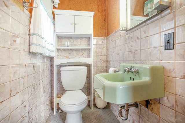 bathroom with toilet, speckled floor, a sink, and tile walls