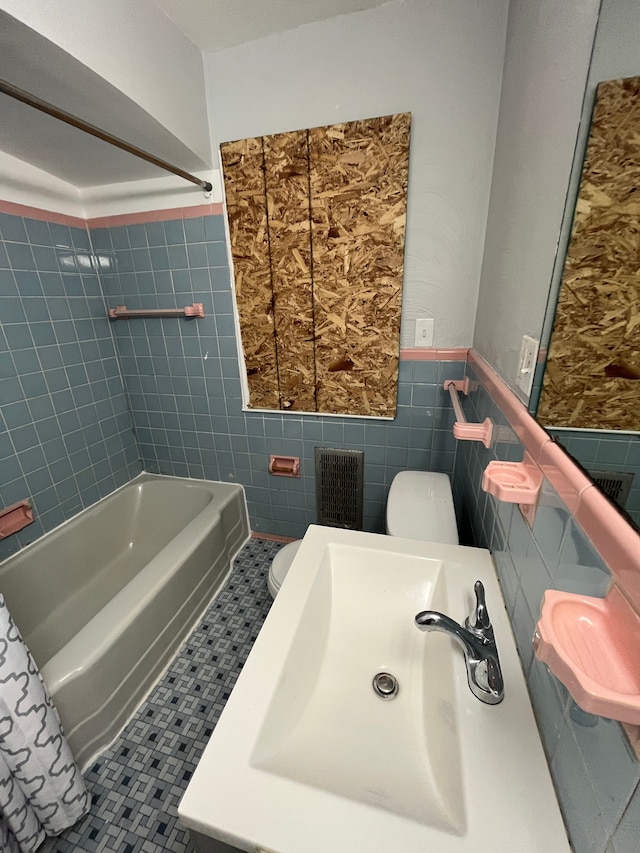 full bathroom featuring tile patterned flooring, toilet, wainscoting, tile walls, and a sink