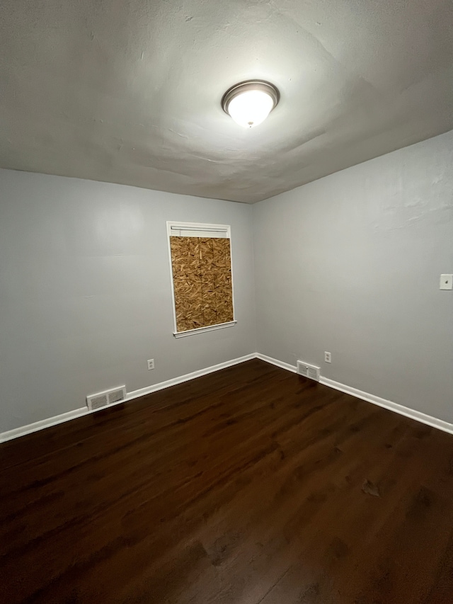 unfurnished room with baseboards, dark wood finished floors, and visible vents