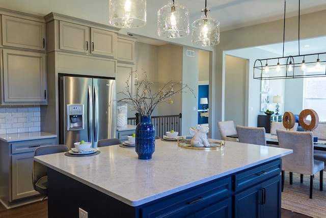 kitchen featuring stainless steel fridge, visible vents, light stone counters, and tasteful backsplash