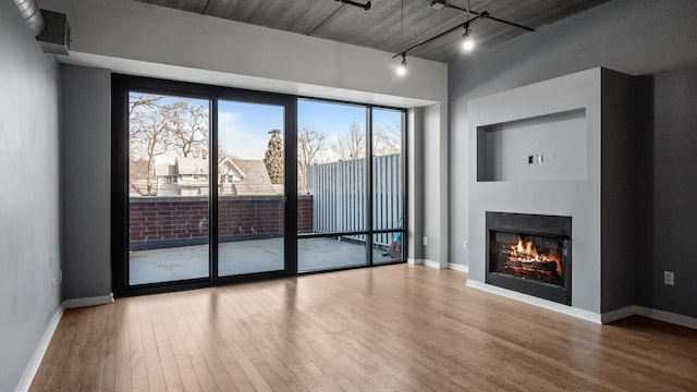 unfurnished living room with a glass covered fireplace, rail lighting, baseboards, and wood finished floors