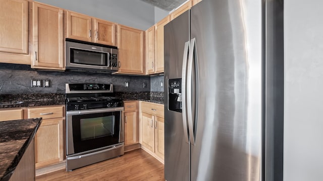 kitchen with stainless steel appliances, light wood-type flooring, light brown cabinetry, tasteful backsplash, and dark stone countertops