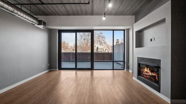 unfurnished living room featuring baseboards, a glass covered fireplace, wood finished floors, a wall of windows, and track lighting