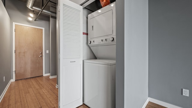 laundry area featuring stacked washer and dryer, baseboards, laundry area, and light wood-style floors