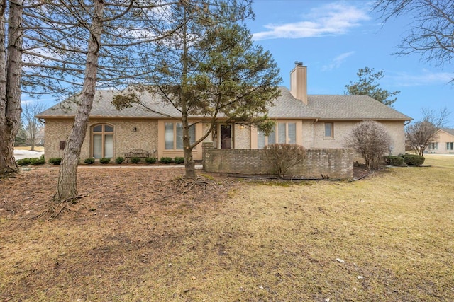 exterior space with a shingled roof, brick siding, a chimney, and a front lawn