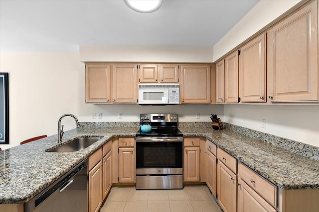 kitchen with stone countertops, a peninsula, a sink, appliances with stainless steel finishes, and light brown cabinetry