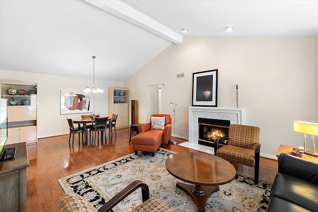 living room featuring lofted ceiling with beams, wood finished floors, visible vents, baseboards, and a high end fireplace