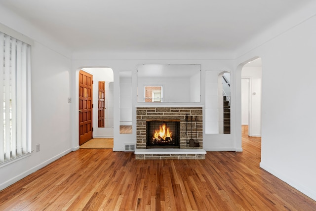 unfurnished living room with arched walkways, visible vents, a stone fireplace, wood finished floors, and baseboards