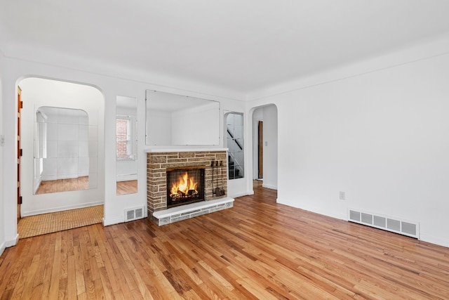 unfurnished living room featuring light wood-style floors, arched walkways, visible vents, and a fireplace