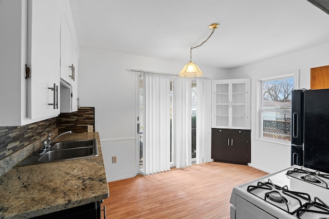 kitchen featuring a sink, light wood-type flooring, freestanding refrigerator, tasteful backsplash, and white gas range