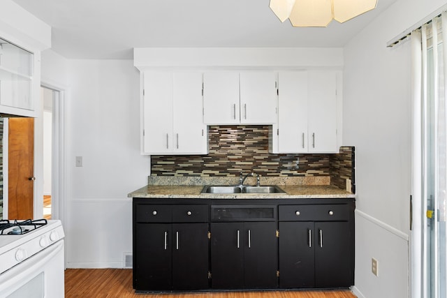 kitchen with dark cabinetry, a sink, backsplash, and white cabinetry