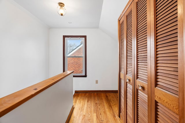 corridor with vaulted ceiling, an upstairs landing, light wood-style flooring, and baseboards