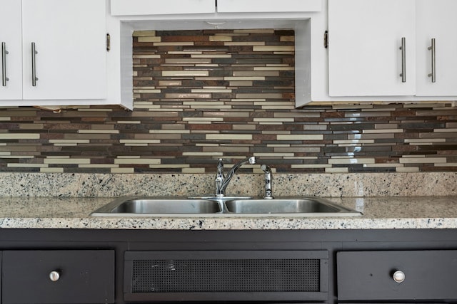 kitchen featuring light stone counters, backsplash, a sink, and white cabinets