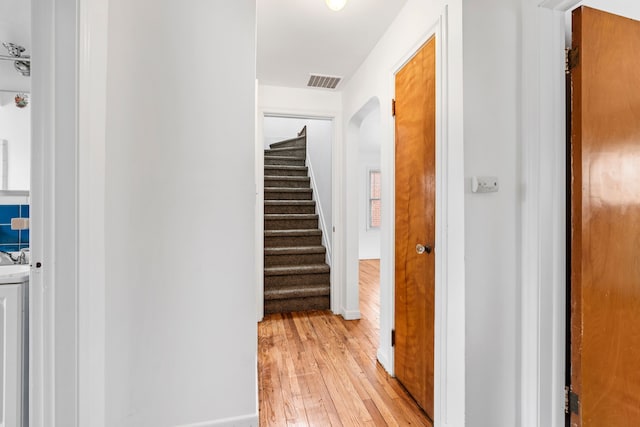 hallway featuring baseboards, visible vents, arched walkways, stairway, and light wood-style floors