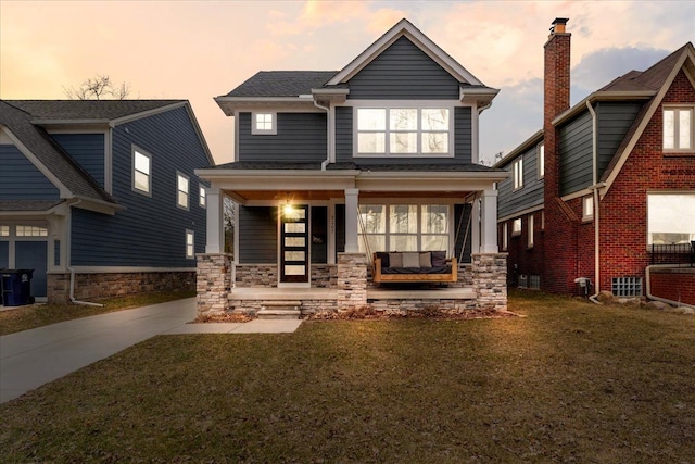 view of front facade featuring stone siding, a porch, and a lawn