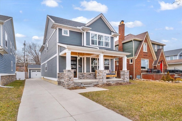 view of front of house featuring stone siding, a detached garage, an outbuilding, covered porch, and a front lawn