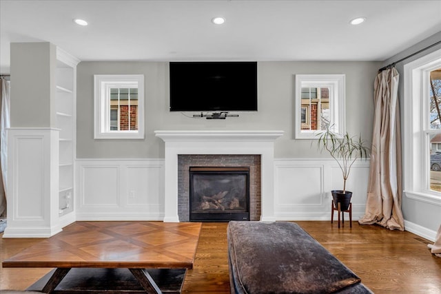 living area featuring wainscoting, wood finished floors, a tiled fireplace, and recessed lighting