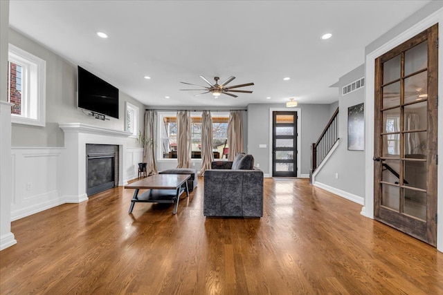 living room with a wealth of natural light, a glass covered fireplace, stairway, and wood finished floors