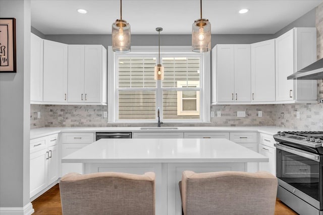 kitchen with a sink, light countertops, appliances with stainless steel finishes, wall chimney exhaust hood, and tasteful backsplash