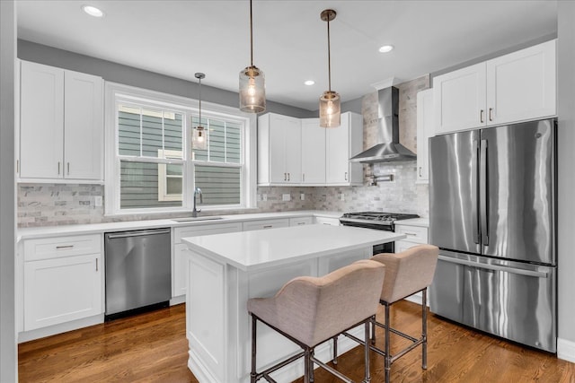 kitchen with appliances with stainless steel finishes, dark wood-type flooring, wall chimney range hood, white cabinetry, and a sink