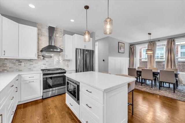 kitchen with a breakfast bar, wall chimney range hood, appliances with stainless steel finishes, and dark wood finished floors