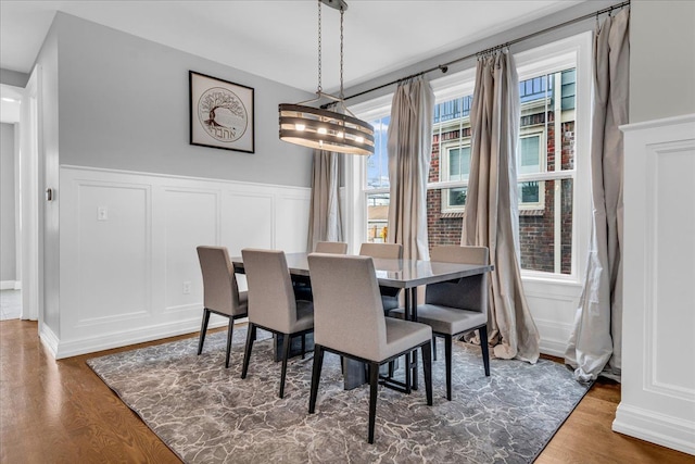 dining area with a wainscoted wall, a decorative wall, and wood finished floors