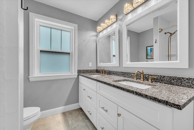 bathroom with toilet, double vanity, baseboards, and a sink