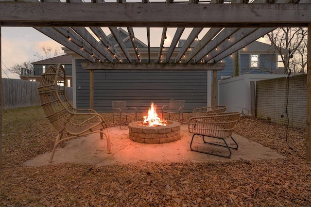 patio terrace at dusk with a fire pit, fence, and a pergola