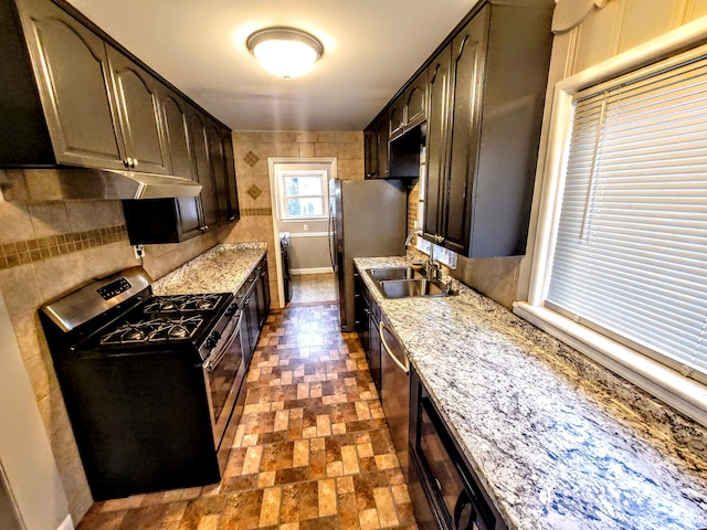 kitchen with under cabinet range hood, stainless steel appliances, a sink, dark brown cabinets, and backsplash