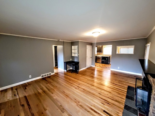 unfurnished living room featuring visible vents, crown molding, baseboards, and wood finished floors