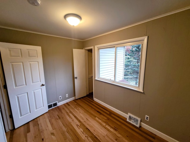 unfurnished bedroom with baseboards, visible vents, wood finished floors, and ornamental molding