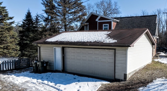 snow covered garage featuring a garage and fence