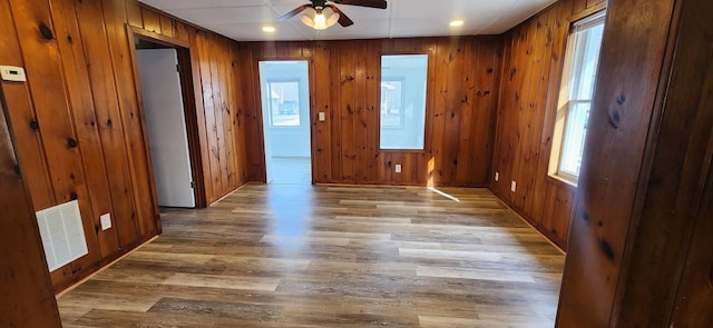 empty room with ceiling fan, wood finished floors, visible vents, and wooden walls