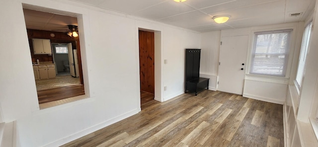 empty room with a wealth of natural light, wood finished floors, visible vents, and baseboards