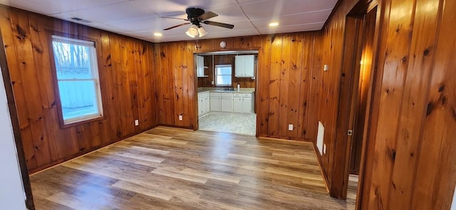 empty room featuring a ceiling fan, visible vents, wooden walls, and light wood finished floors