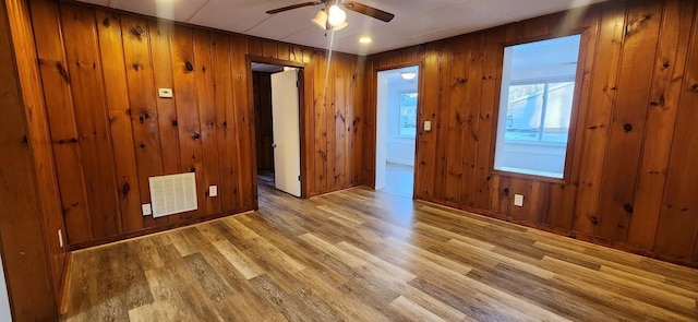 unfurnished room with light wood-type flooring, visible vents, ceiling fan, and wooden walls