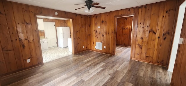 empty room with wood walls, visible vents, ceiling fan, and light wood-style flooring