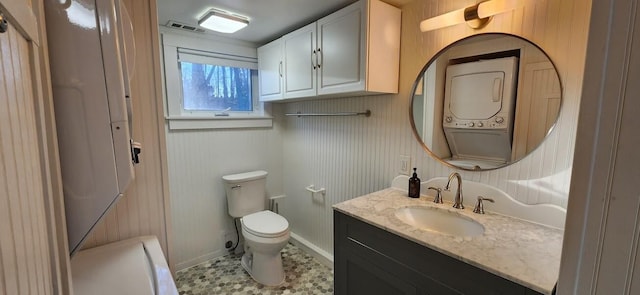 bathroom featuring stacked washer and clothes dryer, visible vents, toilet, vanity, and baseboards