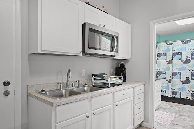 kitchen featuring light countertops, stainless steel microwave, a sink, and white cabinetry