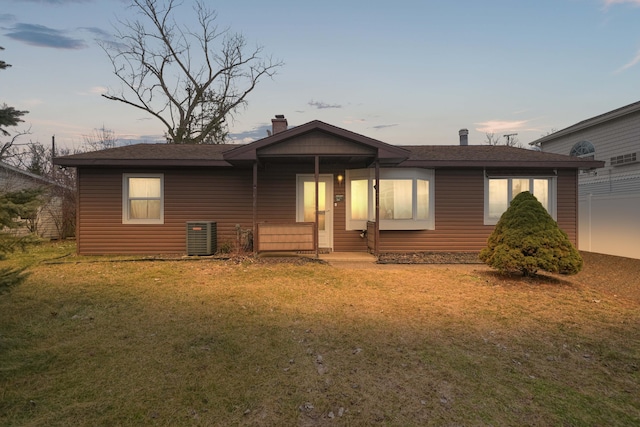 view of front of home featuring a lawn, a chimney, and central air condition unit