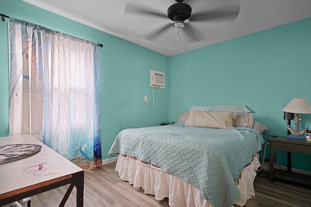 bedroom featuring a wall mounted air conditioner, wood finished floors, a ceiling fan, and baseboards