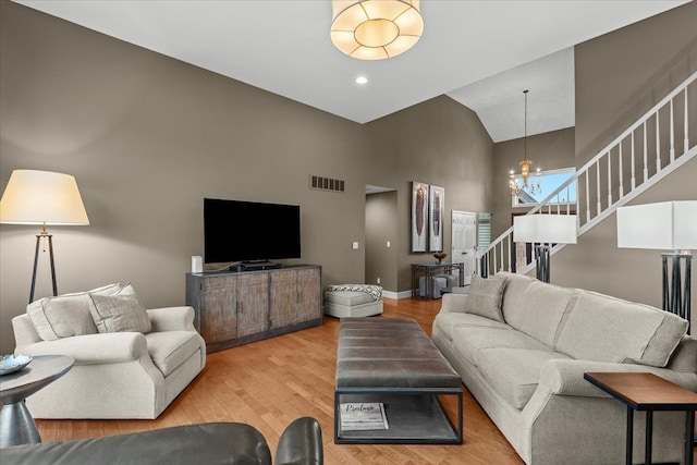 living room featuring high vaulted ceiling, visible vents, stairs, light wood-type flooring, and an inviting chandelier