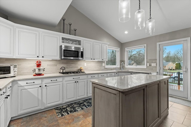 kitchen featuring stainless steel appliances, lofted ceiling, white cabinets, a sink, and light stone countertops