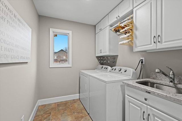 clothes washing area with cabinet space, baseboards, washing machine and clothes dryer, stone finish flooring, and a sink