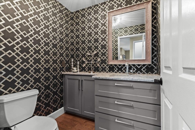 bathroom featuring toilet, wallpapered walls, wood finished floors, and vanity